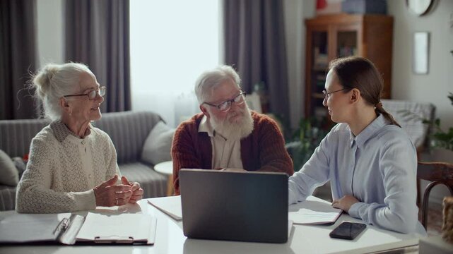 Female financial advisor in formal shirt helping elderly couple with documents and bills, explaining information on laptop and answering their questions during consultation at home