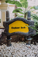 A 'Elephant Deck' sign post that seems like it's made from a tree trunk - in yellow background