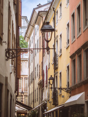 A charming narrow street in Udine, Italy, lined with colorful historic buildings, ornate lamps, and shuttered windows. The warm hues and classic architecture evoke a timeless European atmosphere.
