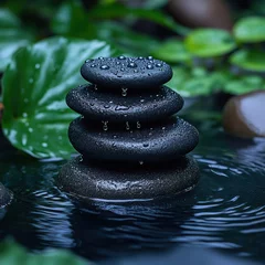 Stack of hot stones with drops of water and tropical leaves in background