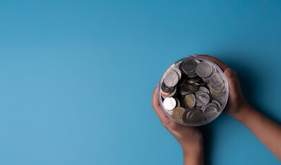 Save money for investment concept Hand holding jar of coins on a blue background.