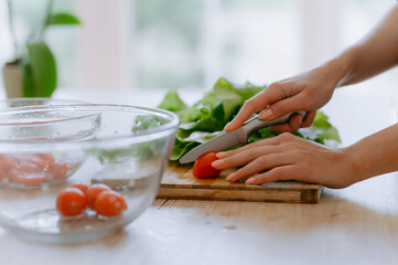 A person is skillfully slicing ripe tomatoes on a wooden cutting board alongside fresh greens, highlighting the essence of healthy cooking.