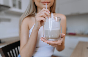 Young woman sips on a delicious, creamy drink in a modern kitchen setting, capturing the essence of...