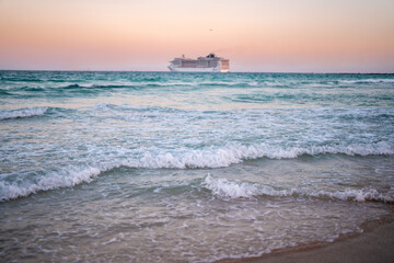Fototapeta premium Cruise ship on the ocean. Luxury liner at sunset. Miami Beach with cruise ship. Turquoise water and cruise liner. Tourist cruise ship near the coast. Ocean waves and vessel boat.