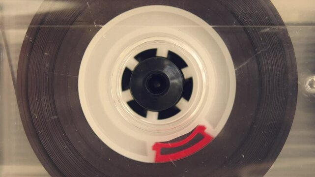 Extreme closeup of spinning cassette reel evokes retro aesthetic and analog sound era, capturing rhythm and texture of the nostalgic 90s.