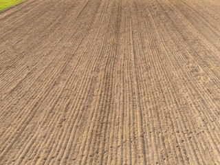 Aerial view of freshly plowed agricultural field, displaying neat parallel rows of soil ready for planting, highlighting agriculture and rural landscape.