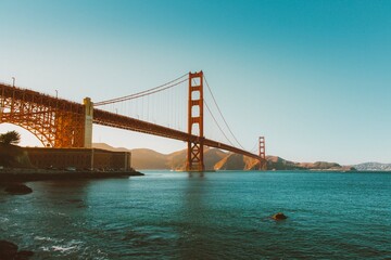 Golden suspension bridge over calm blue waters at sunset