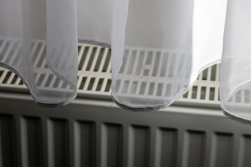 Sheer white curtains gently draping over a heater, creating a soft atmosphere in an indoor setting,...