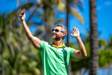 Tourist takes a selfie near palm tree. Man traveler captures a selfie during summer vacation. Traveler snaps a selfie in a tropical destination. A selfie with palm trees captures the tropical vibes.
