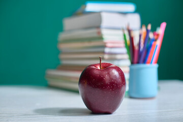Red apple placed on a desk with a stack of books and colorful pencils in the background, representing education, school, and teacher appreciation elements.