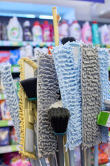 Various cleaning tools, including mops and brushes, are organized and displayed in a store aisle....