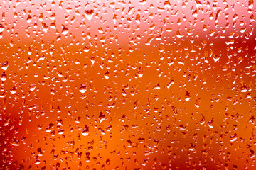 Photograph of raindrops on a glass surface reflecting and distorting a vibrant and colourful background capturing the beauty of light and water and sunlight.