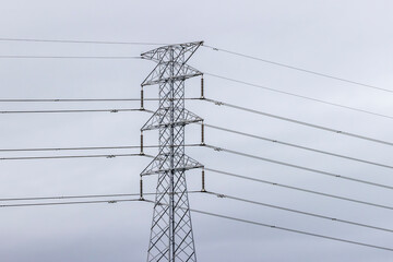 Photograph of the intricate and complex lattice steel work on the upper section of a large Transmission Tower against a cloudy grey sky.