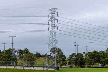 Obraz premium Photograph of a Transmission Tower located near a fence and an array of lighting towers amongst trees and other infrastructure in a green field.