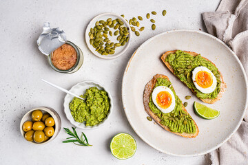 Toast with fresh avocado, eggs, herbs and seeds with lemon slices on white background. Healthy eating and wholesome Breakfast, top view