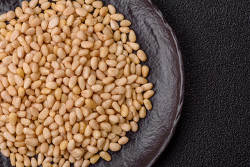 Peeled pine nuts in a bowl on a dark concrete background