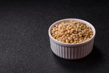 Peeled pine nuts in a bowl on a dark concrete background