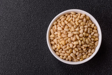 Peeled pine nuts in a bowl on a dark concrete background