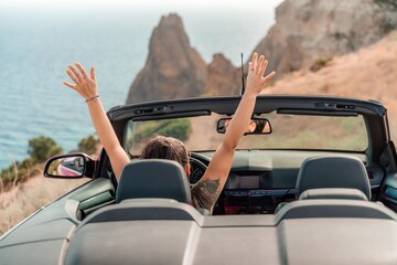 A woman is driving a convertible car on a mountain road, waving her hands in the air. Concept of...