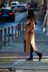 Walking confidently on a chilly street in a stylish coat, a woman enjoys the crisp air and urban...