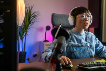 A professional, beautiful Asian female gamer is sitting in front of her PC, visibly upset after losing an online game. Her frustration is evident as she reflects on the gameplay. © Nenad