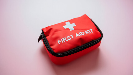 A red first aid kit with a white cross symbol is prominently on a vibrant pink surface, indicating its purpose for health care and emergency assistance, ensuring readiness when needed
