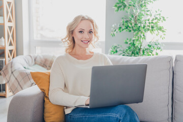 Smiling Young Blonde Woman Working Comfortably on Laptop at Home in a Cozy Living Room Setting During Daylight