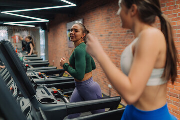 Fototapeta premium Two young women running on treadmills in modern gym