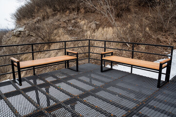 There are two wooden benches placed on a sturdy metal platform that features a safety railing,...