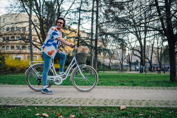 Fototapeta premium Stylish man riding bicycle in urban park, enjoying music and carrying groceries