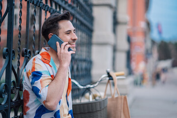 Fototapeta premium Young man talking on smartphone leaning on a gate with his bicycle nearby