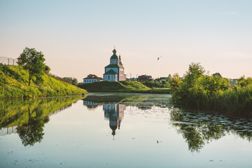 Fototapeta premium Peaceful countryside landscape with historic Orthodox church rises above lush greenery and a reflective river