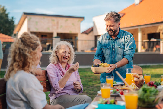 Happy family enjoying backyard meal together, serving fruit platter - Powered by Adobe