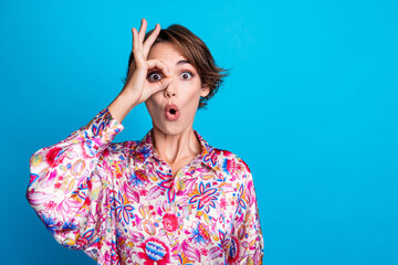 Photo of astonished funky girl wear stylish print clothes look through binoculars okey sign empty...