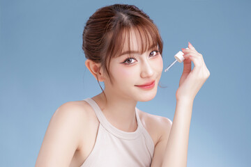 Obraz premium Beautiful young Asian woman model with bangs and natural makeup on face clean fresh skin using dropper for apply serum on isolated blue background. Facial treatment, Body care, Beauty and Spa.