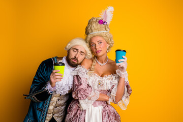 Elegant couple dressed in vintage costumes enjoying coffee together against vibrant yellow backdrop