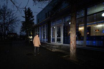 Evening stroll towards a cozy cafe adorned with twinkling lights and a warm ambiance on a tranquil winter night