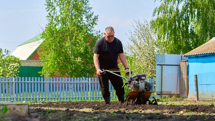 A man is working in a field with a tractor. The field is surrounded by a fence and a house is visible in the background