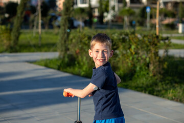 Boy with diabetes riding a scooter, looking back, smiling at the camera.