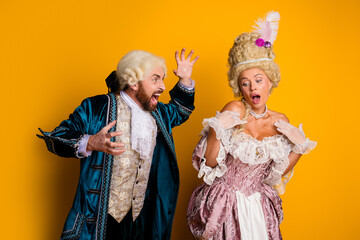 Historical couple in aristocratic outfits reacting theatrically against vibrant yellow backdrop