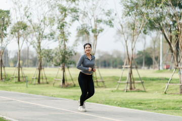 A young woman is jogging in a city park, surrounded by lush trees that provide shade and a refreshing atmosphere.