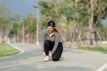 Fototapeta premium A young woman pauses during her run to tighten her shoelaces. A gentle breeze and birdsong refresh her before she stretches and continues running.