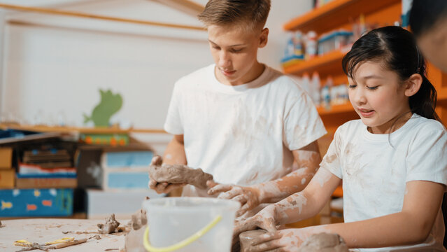 Caucasian boy modeling bowl of clay while cute asian girl working on dough at pottery workshop. Skilled highschool student playing on dough while wear muddy shirt at art lesson. Creative. Edification.