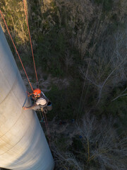 Worker inspecting concrete chimney using descending techniques in forest area