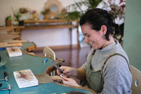 Jeweler filing metal in workshop creating jewelry