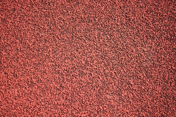 Red sports field rubber coating close up macro view. Playground paving background texture extremely close.