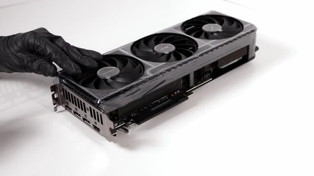 Person in black gloves removing protective film from ASUS GeForce RTX graphics card with triple fan design on white background