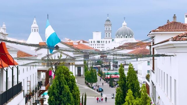 Guatemala, Guatemala. March 17, 2025: A Guatemalan flag flies in the middle of the new Cayala City. A premium neighborhood on the outskirts of the capital. The dome of a church stands in the back.