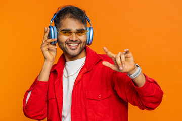 Portrait of happy stylish Indian man in sunglasses listening music via headphones, dancing disco...