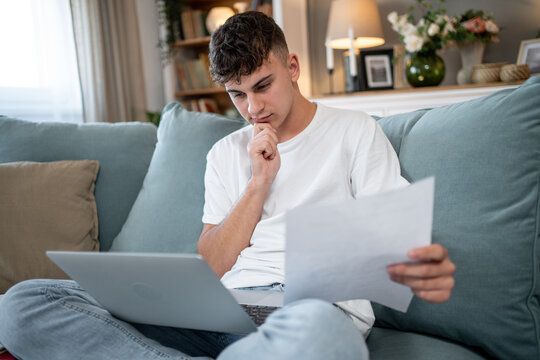 Focused teenager managing finances on laptop with documents at home